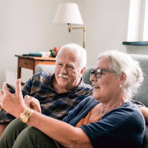 Vanha pariskunta olohuoneessa lukemassa kännykän ruutua